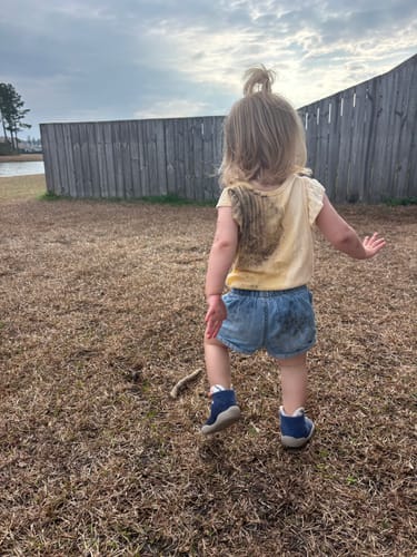 Criança caminhando na grama com tênis-meia azul