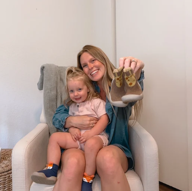 Mãe com a filha no colo mostrando um par de tênis-meia