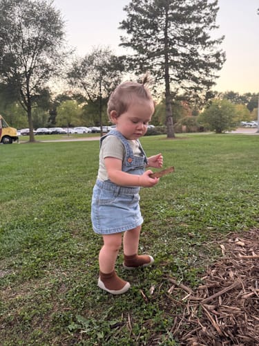 Criança de jardineira usando tênis-meia marrom no parque